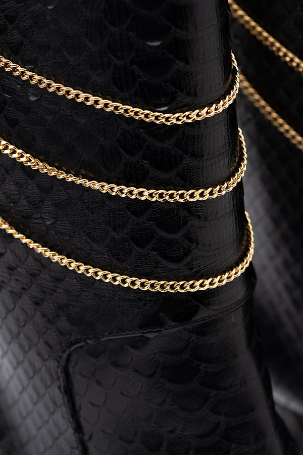 Zoom in on the black boots with gold chain of the Naomi Black Python Print Boot