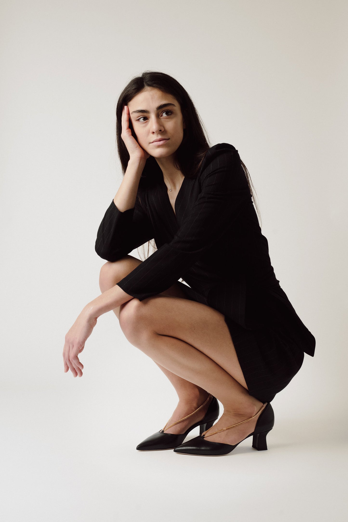 Thinking woman neeling wearing black suit and the Linda Black Dorsay shoes