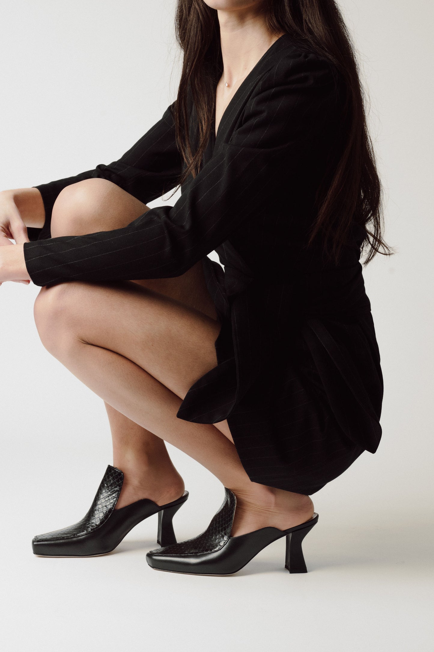 woman neeling in a grey room wearing cute mule shoes (Black)