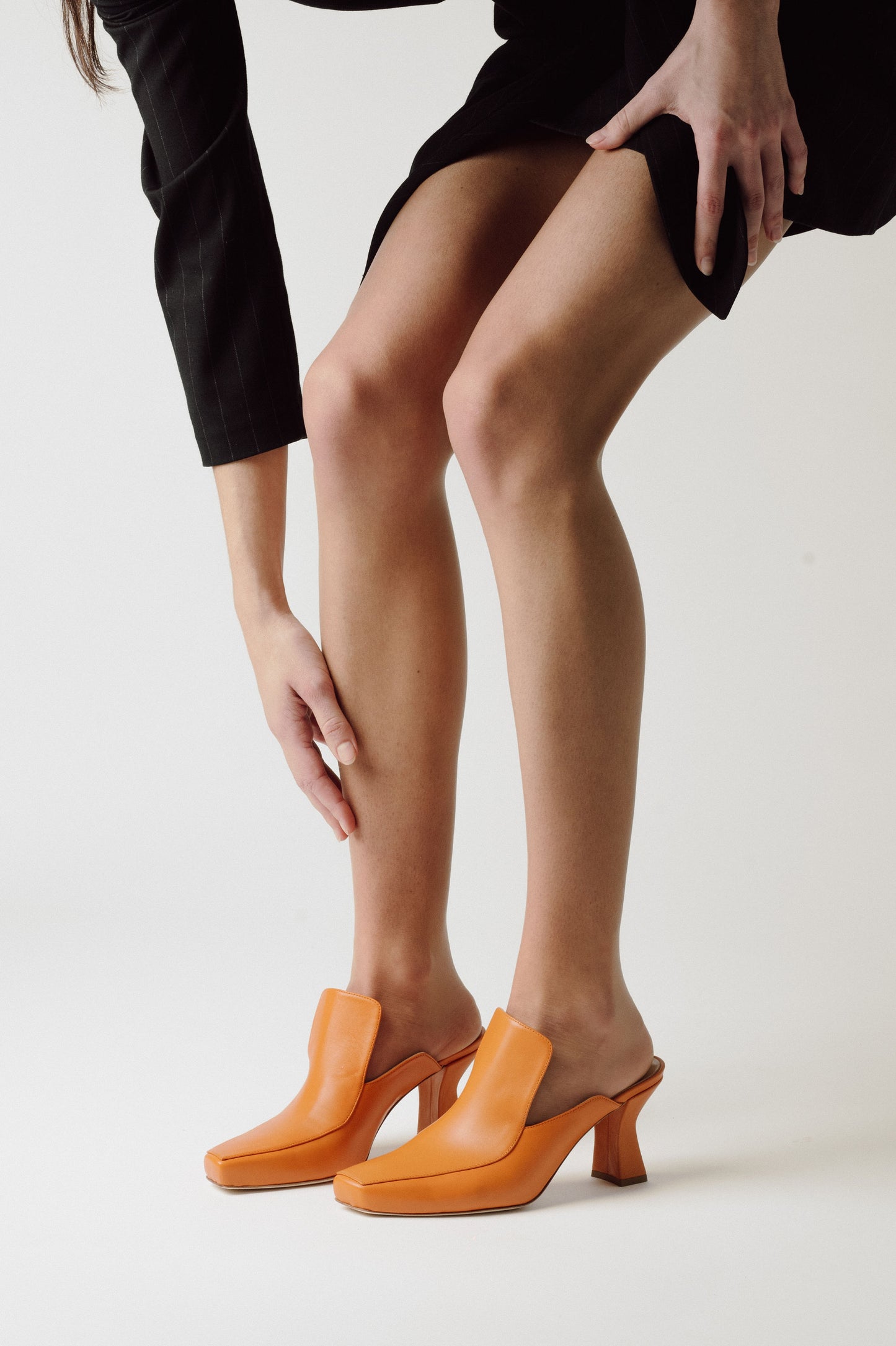 woman bending towards her's cute brown mule shoes in a grey room